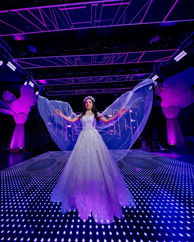 Quinceañera con alas de luz en la pista iluminada