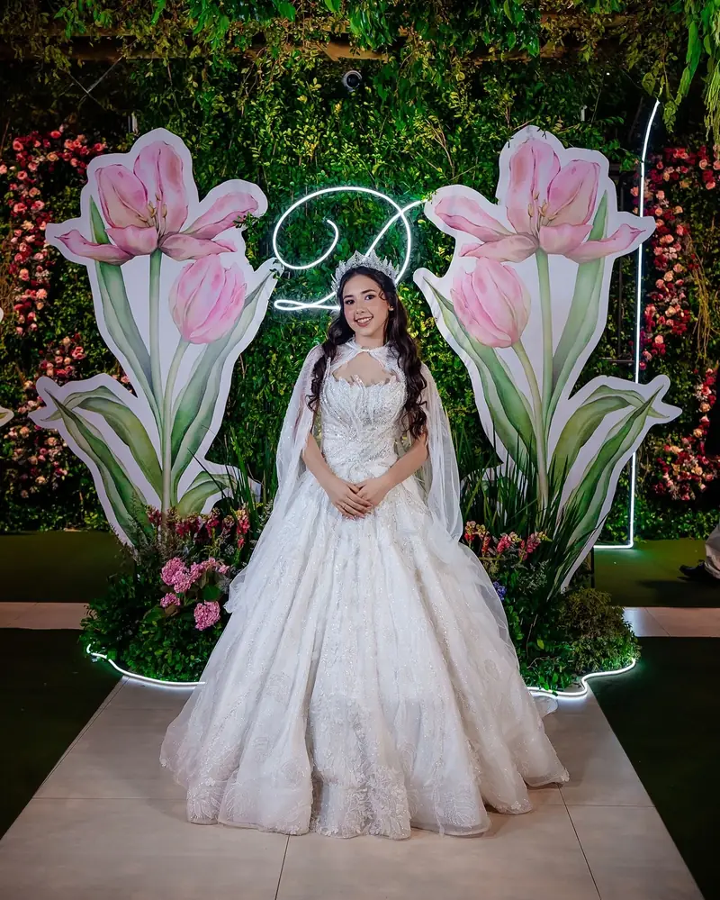 Quinceañera con vestido largo blanco entre flores gigantes