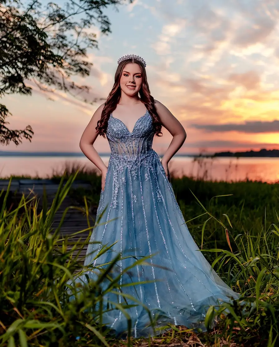 Quinceañera con vestido azul brillante frente al agua al atardecer