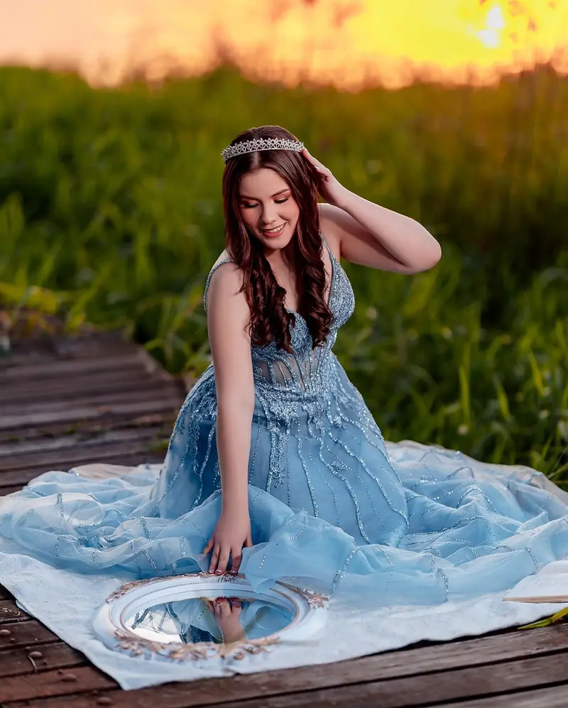 Quinceañera con vestido azul sobre el pasto junto al agua